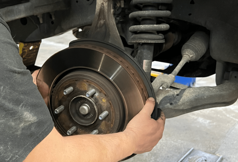 Brake Repair in York, PA with Quality Service Center. Image of a mechanic inspecting brake rotor and brake pad replacement for a gray lifted car.